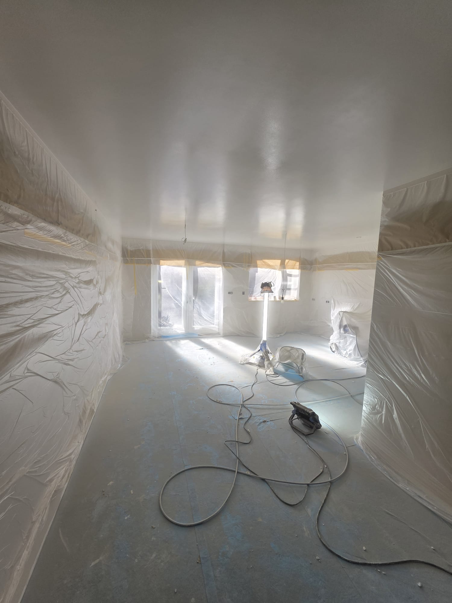 Ruime kamer met afgeplakte wanden en een vers afgewerkt plafond, met bouwlamp