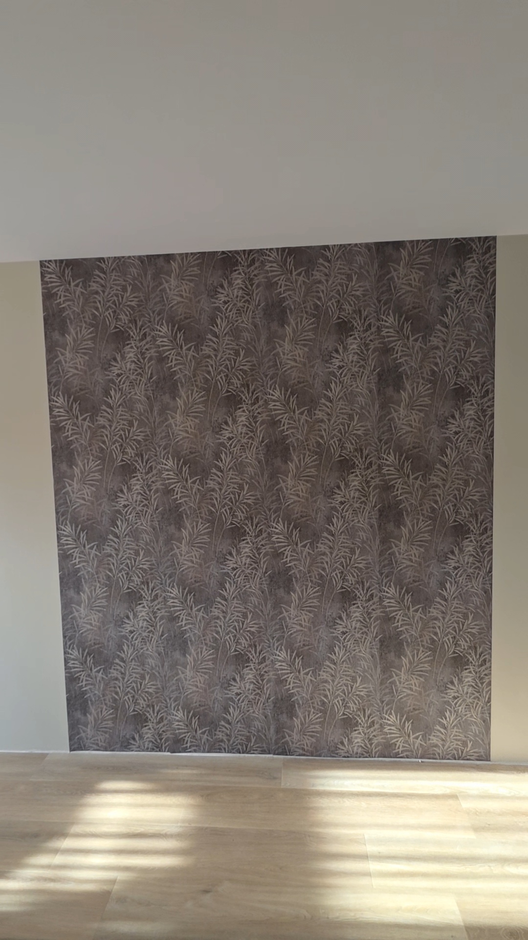 Accentwand met donker behang met bladmotief boven een houten vloer