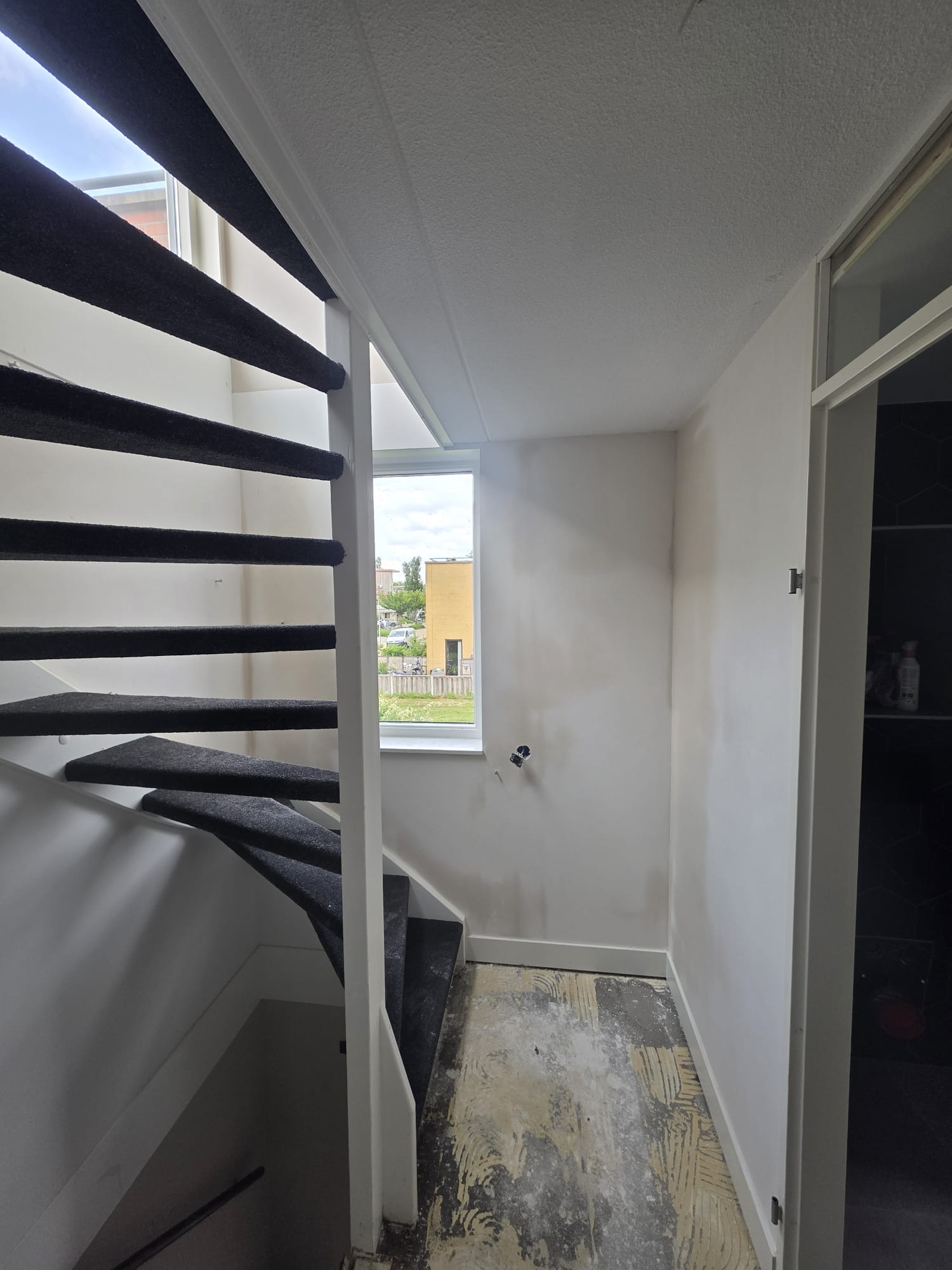 Overloop met zwarte open trap en strakke witte wanden, nog in uitvoering